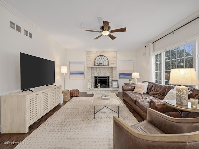 living room featuring ceiling fan, ornamental molding, wood-type flooring, and a stone fireplace