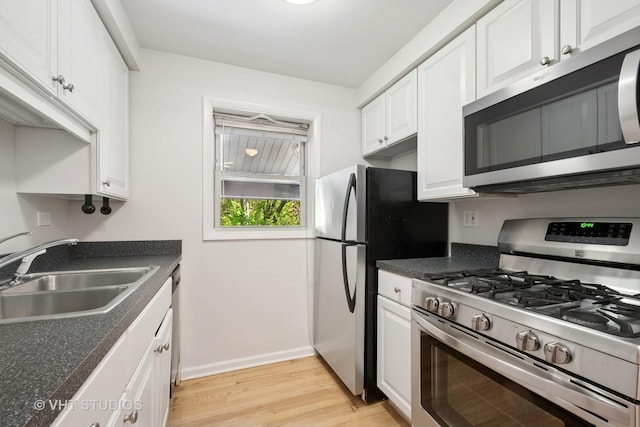 kitchen featuring appliances with stainless steel finishes, a sink, white cabinetry, and light wood-style floors