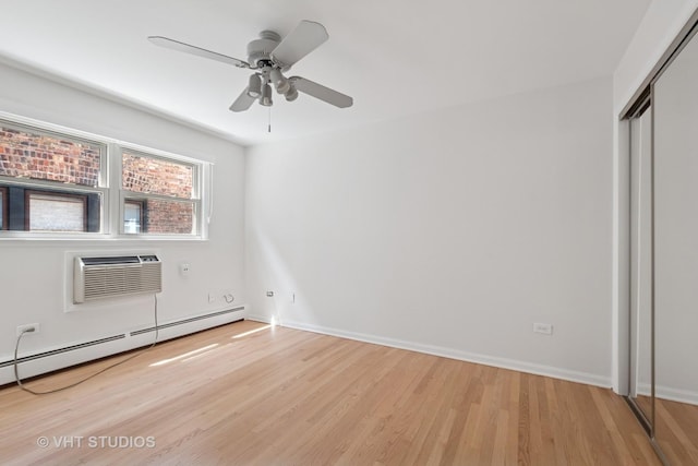 unfurnished bedroom with a baseboard heating unit, a wall mounted air conditioner, light wood-style flooring, a closet, and baseboards