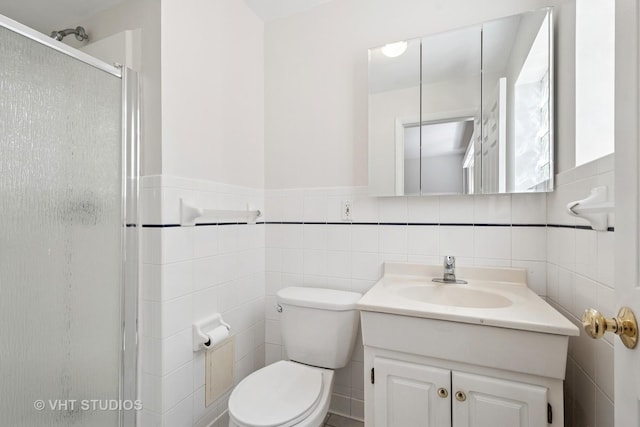 full bathroom with a shower stall, tile walls, vanity, toilet, and a wainscoted wall