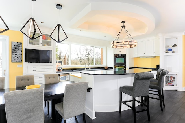 kitchen with white cabinets, a kitchen bar, hanging light fixtures, black double oven, and dark wood-type flooring