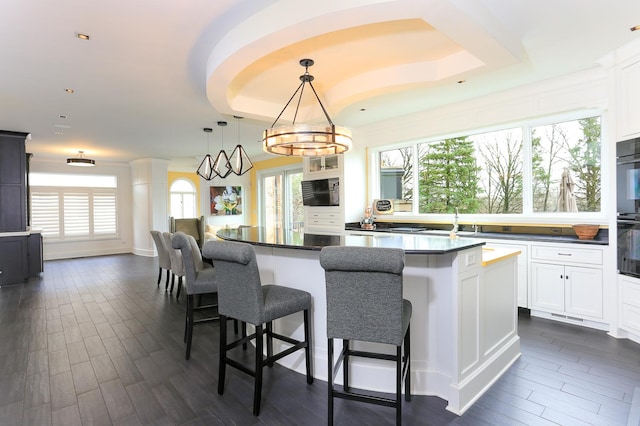 kitchen with a breakfast bar, a wealth of natural light, white cabinetry, hanging light fixtures, and a center island