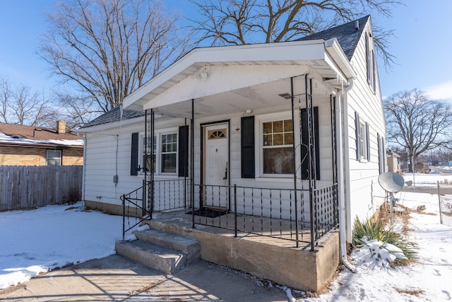 bungalow-style home with a shingled roof and fence