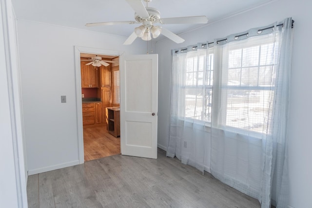 spare room with light wood-type flooring, a ceiling fan, and baseboards