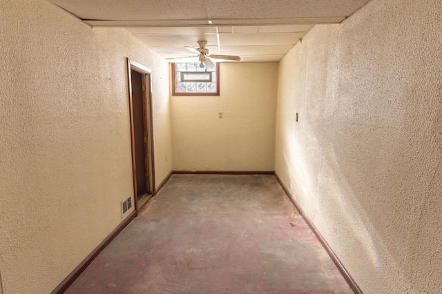 corridor featuring a textured wall, concrete floors, visible vents, and baseboards