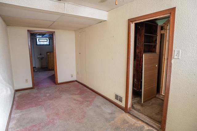 empty room featuring baseboards, visible vents, a drop ceiling, and a textured wall