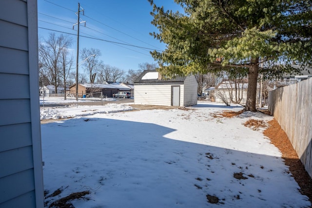 snowy yard featuring a shed, an outdoor structure, and fence