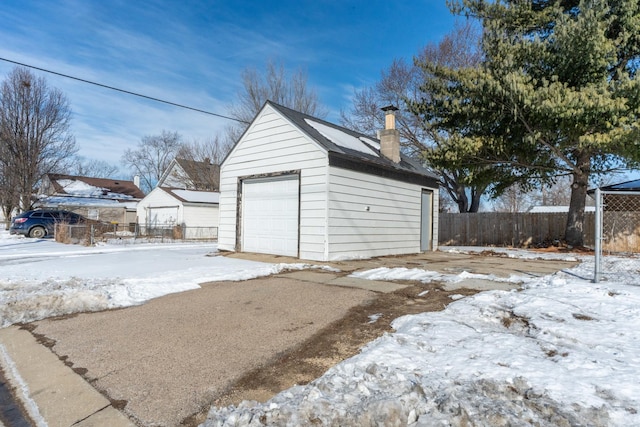 snow covered garage with a detached garage and fence