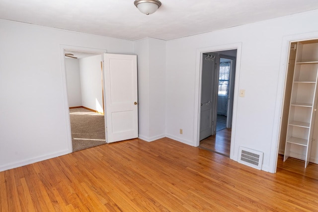 empty room with light wood-style flooring, visible vents, and baseboards