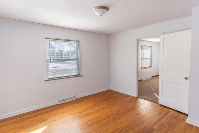 unfurnished room featuring light wood-type flooring, visible vents, and baseboards