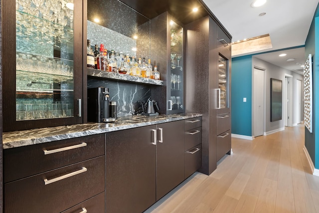 bar with light stone counters, light wood-type flooring, and backsplash