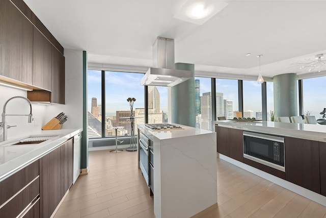 kitchen with sink, black microwave, light stone counters, island range hood, and light wood-type flooring