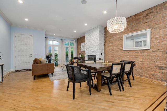 dining space with brick wall, a stone fireplace, ornamental molding, a notable chandelier, and light hardwood / wood-style floors