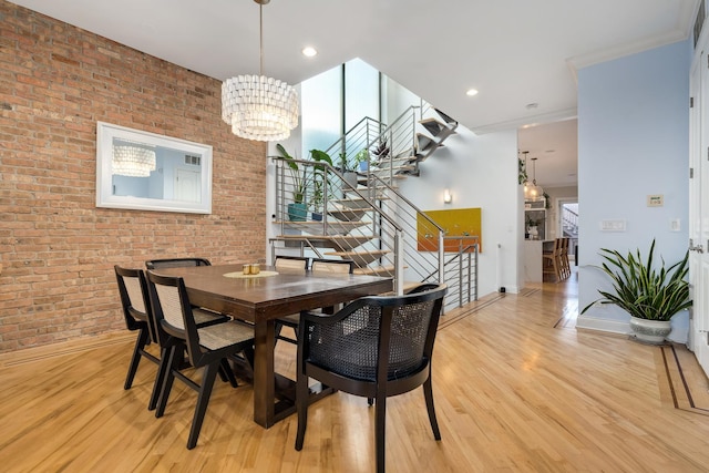 dining space featuring an inviting chandelier, brick wall, crown molding, and light hardwood / wood-style flooring