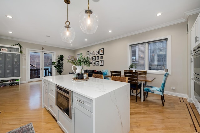 kitchen with pendant lighting, white cabinets, wall oven, and light hardwood / wood-style flooring