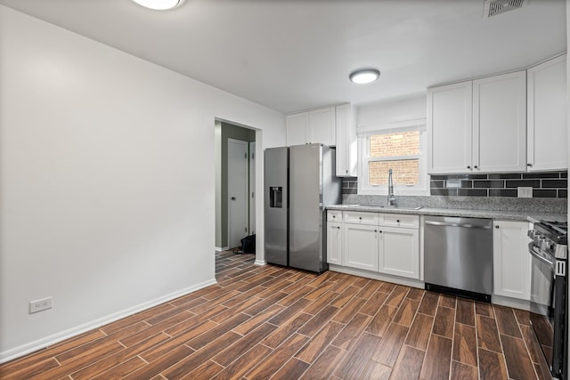 kitchen with sink, white cabinetry, stainless steel appliances, light stone countertops, and decorative backsplash