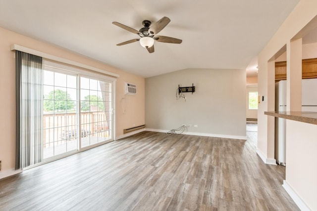 unfurnished room featuring light hardwood / wood-style flooring, an AC wall unit, a healthy amount of sunlight, and vaulted ceiling