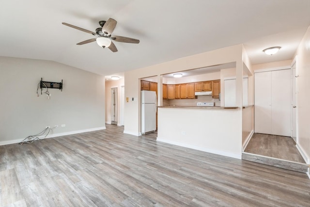 interior space featuring vaulted ceiling, kitchen peninsula, white fridge, ceiling fan, and light hardwood / wood-style floors