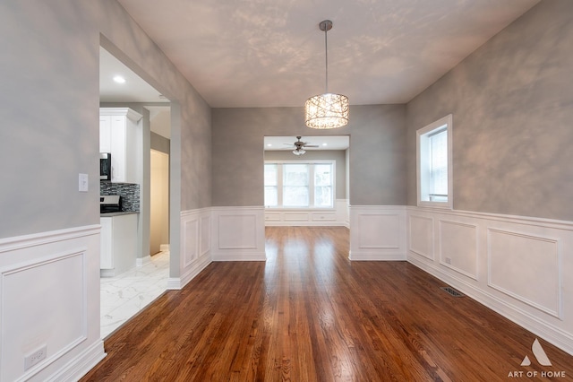 unfurnished dining area with dark wood-type flooring and ceiling fan with notable chandelier