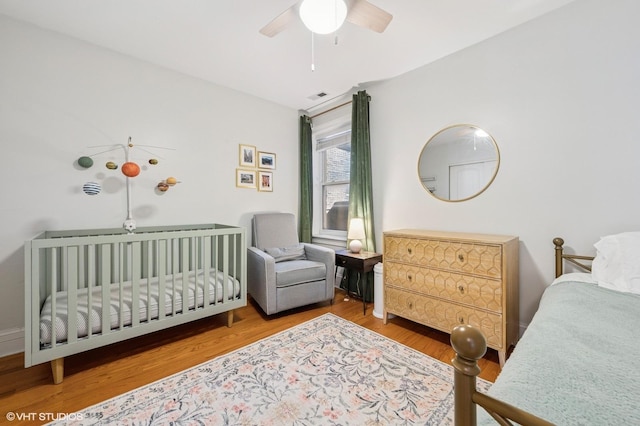 bedroom featuring visible vents, ceiling fan, a crib, and wood finished floors