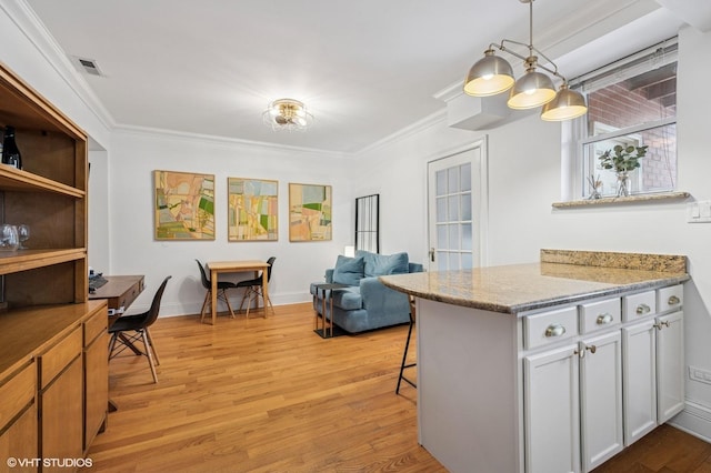 kitchen with light wood finished floors, visible vents, a breakfast bar, crown molding, and pendant lighting