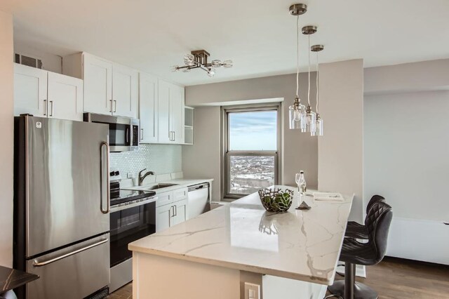 kitchen featuring stainless steel appliances, light stone counters, white cabinets, a kitchen island, and decorative light fixtures