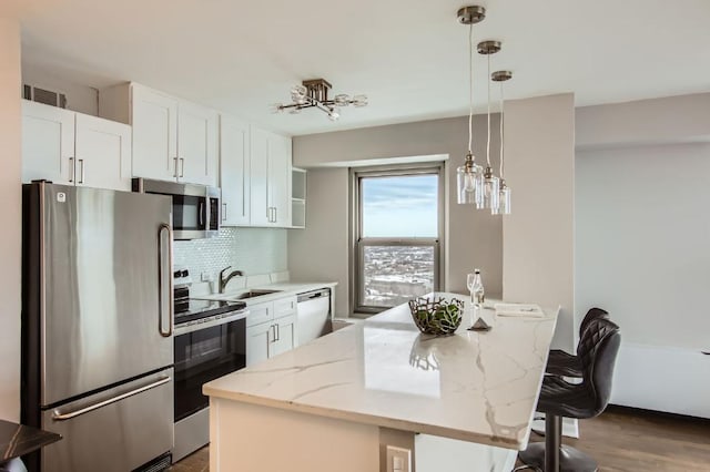 kitchen with a kitchen island, light stone counters, stainless steel appliances, white cabinetry, and pendant lighting