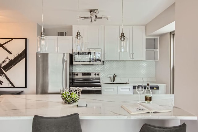 kitchen with stainless steel appliances, a sink, a kitchen breakfast bar, white cabinets, and hanging light fixtures