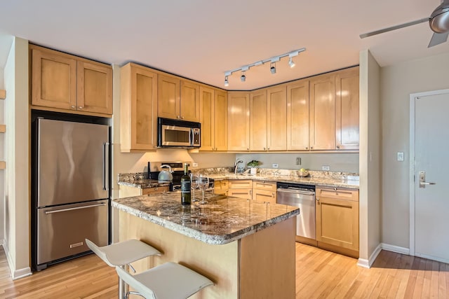 kitchen featuring dark stone countertops, light hardwood / wood-style floors, stainless steel appliances, and a kitchen breakfast bar