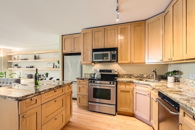 kitchen with appliances with stainless steel finishes, light brown cabinetry, sink, light stone countertops, and light wood-type flooring