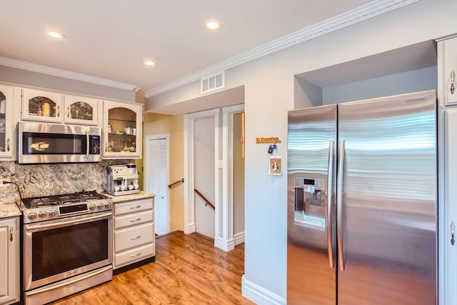 kitchen with appliances with stainless steel finishes, backsplash, white cabinets, light hardwood / wood-style floors, and crown molding