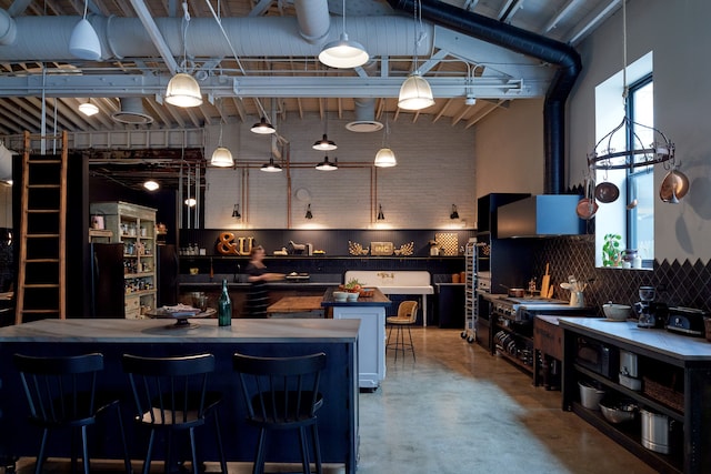 kitchen with black refrigerator, tasteful backsplash, concrete floors, and a towering ceiling