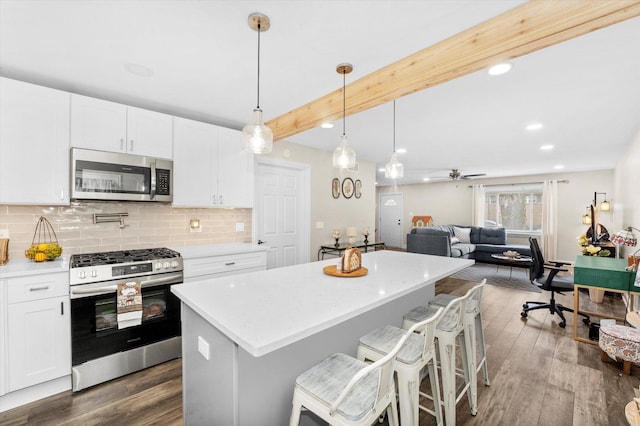 kitchen with a kitchen bar, white cabinetry, decorative light fixtures, appliances with stainless steel finishes, and beam ceiling