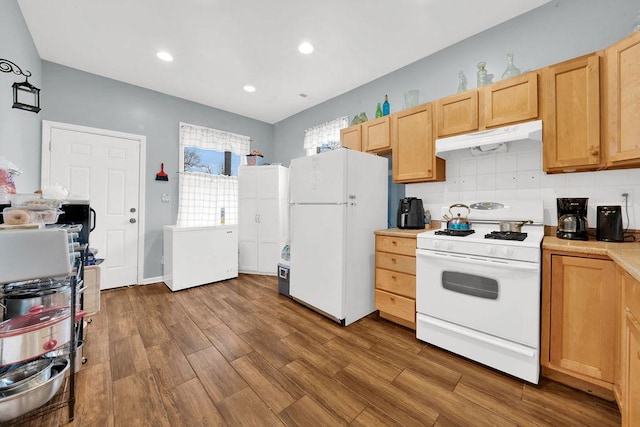 kitchen with light countertops, white appliances, under cabinet range hood, wood finished floors, and decorative backsplash