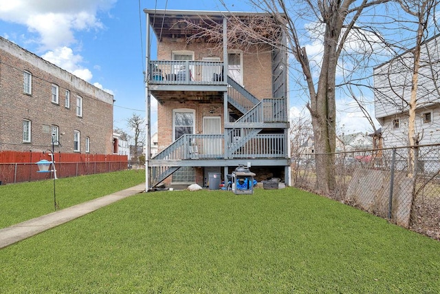 rear view of house with a yard, brick siding, a fenced backyard, and stairway
