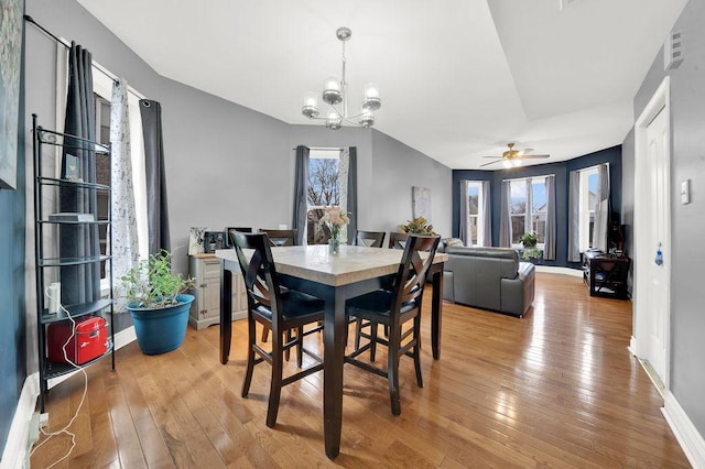 dining area with light wood-style flooring, ceiling fan with notable chandelier, and baseboards