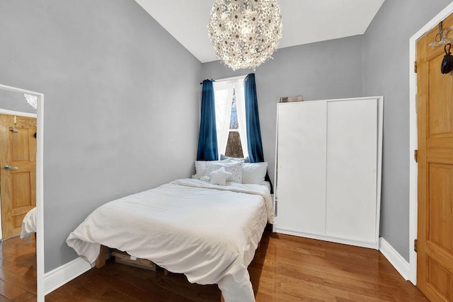 bedroom with baseboards, vaulted ceiling, a notable chandelier, and wood finished floors