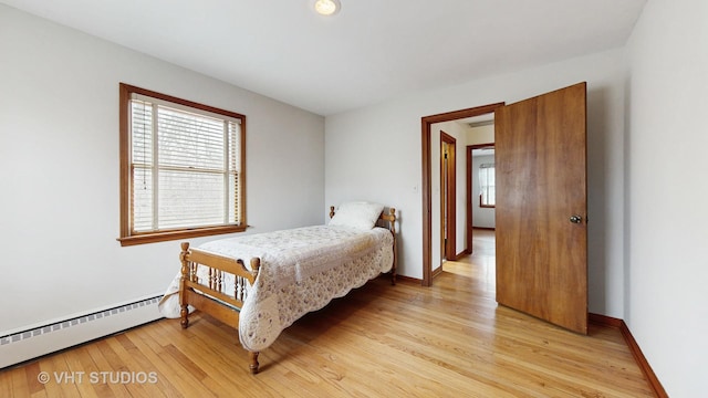 bedroom featuring a baseboard heating unit, baseboards, multiple windows, and light wood finished floors