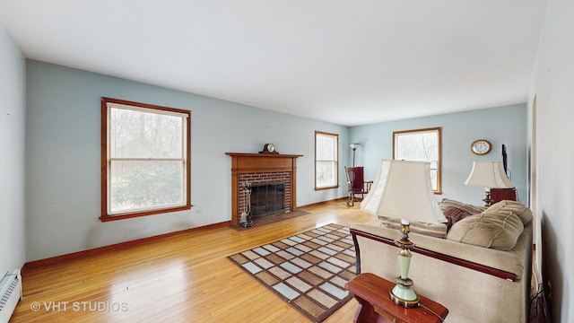 living area featuring a brick fireplace, baseboards, light wood finished floors, and baseboard heating