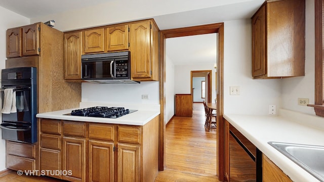 kitchen featuring a warming drawer, black appliances, light countertops, and brown cabinets