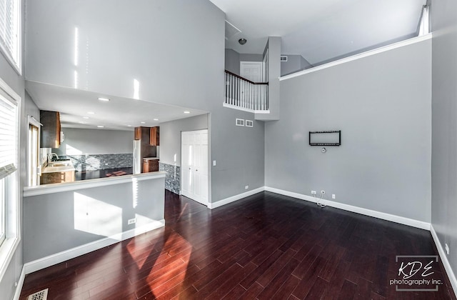 unfurnished living room featuring sink, wood-type flooring, and a high ceiling