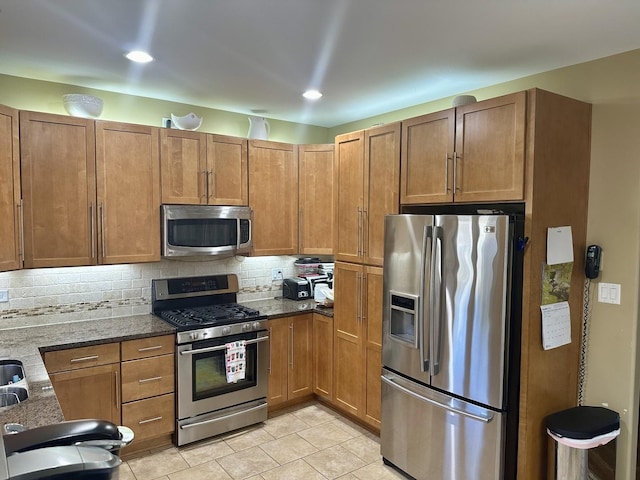 kitchen featuring tasteful backsplash, appliances with stainless steel finishes, dark stone countertops, and light tile patterned floors