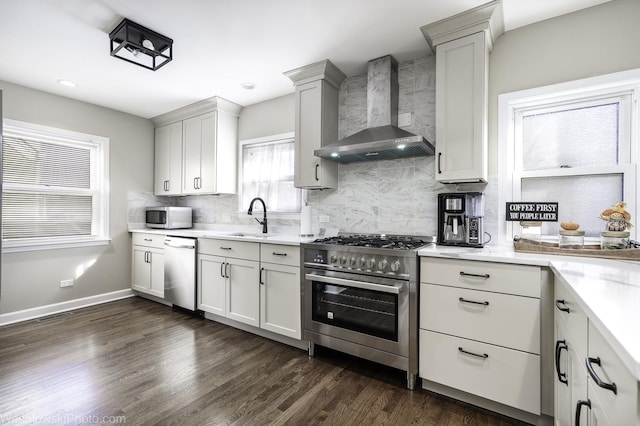 kitchen with appliances with stainless steel finishes, tasteful backsplash, sink, white cabinets, and wall chimney range hood