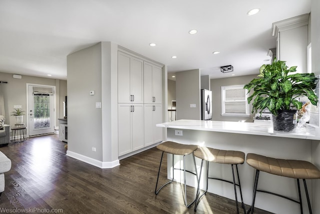 kitchen featuring dark hardwood / wood-style flooring, stainless steel fridge, light stone countertops, and a kitchen bar