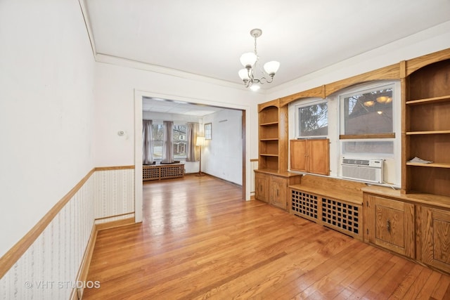 interior space featuring crown molding, cooling unit, built in shelves, a chandelier, and light wood-type flooring