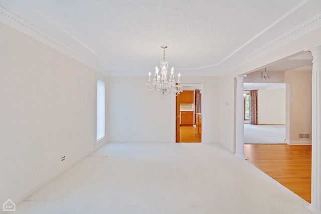 empty room featuring ornate columns, hardwood / wood-style floors, a notable chandelier, crown molding, and a textured ceiling