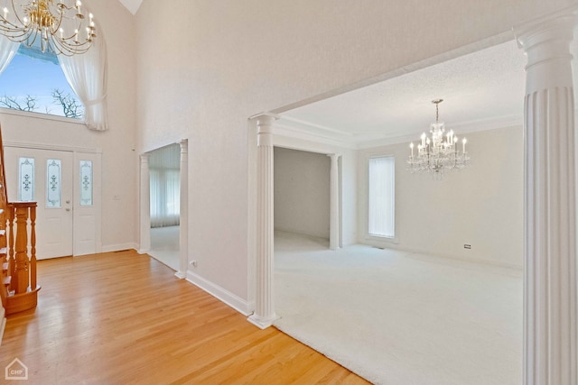 entryway featuring a notable chandelier, wood-type flooring, ornamental molding, and ornate columns