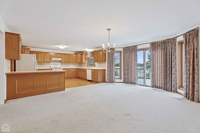 kitchen featuring pendant lighting, a chandelier, kitchen peninsula, light carpet, and white appliances