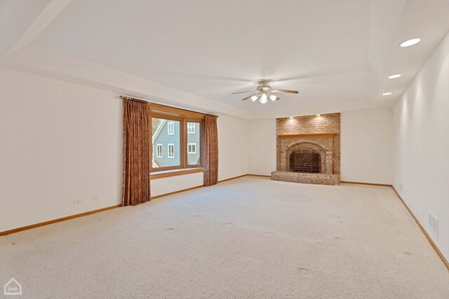 unfurnished living room with ceiling fan, a raised ceiling, carpet, and a brick fireplace