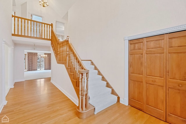 stairs with hardwood / wood-style flooring, high vaulted ceiling, and an inviting chandelier